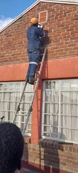 Wikilax Tech Solutions technician installing a security camera on a brick building